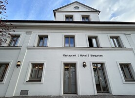 Um edifício branco com uma placa que diz "Restaurante | Hotel | Biergarten" e várias janelas.