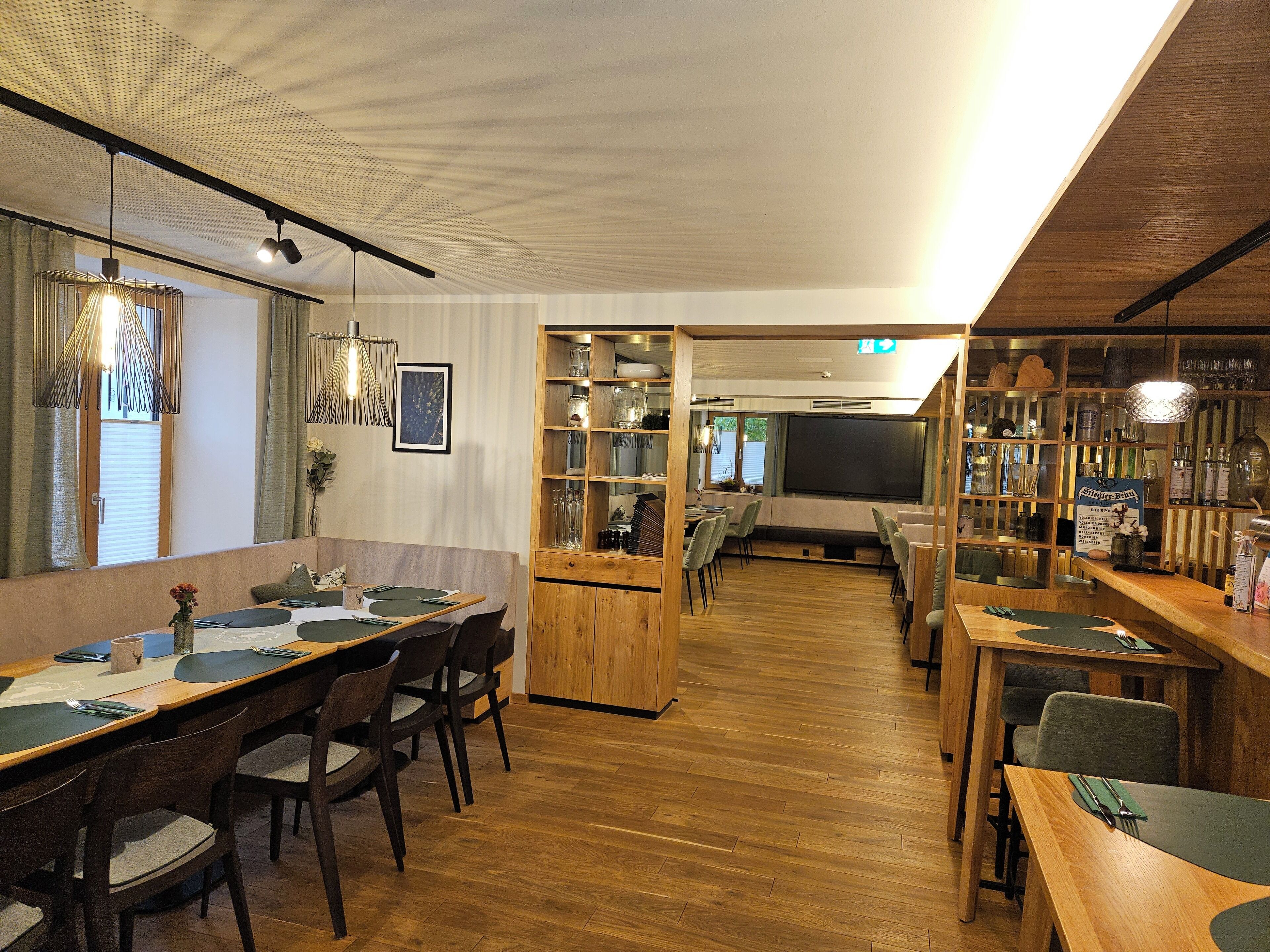 A restaurant with wooden tables and chairs, a bar area, and a projection screen.