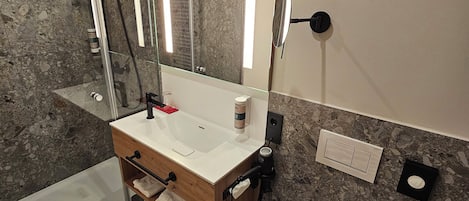 A modern bathroom with a glass shower enclosure, a wooden vanity, a white sink, and a marble-tiled floor.