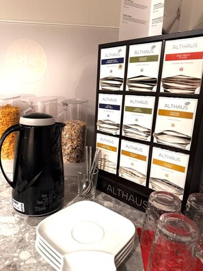 A tea station with a black kettle, tea bags, and a signboard displaying various tea brands and flavors. - Stieglers - Restaurant Hotel Biergarten (Ergoldsbach)