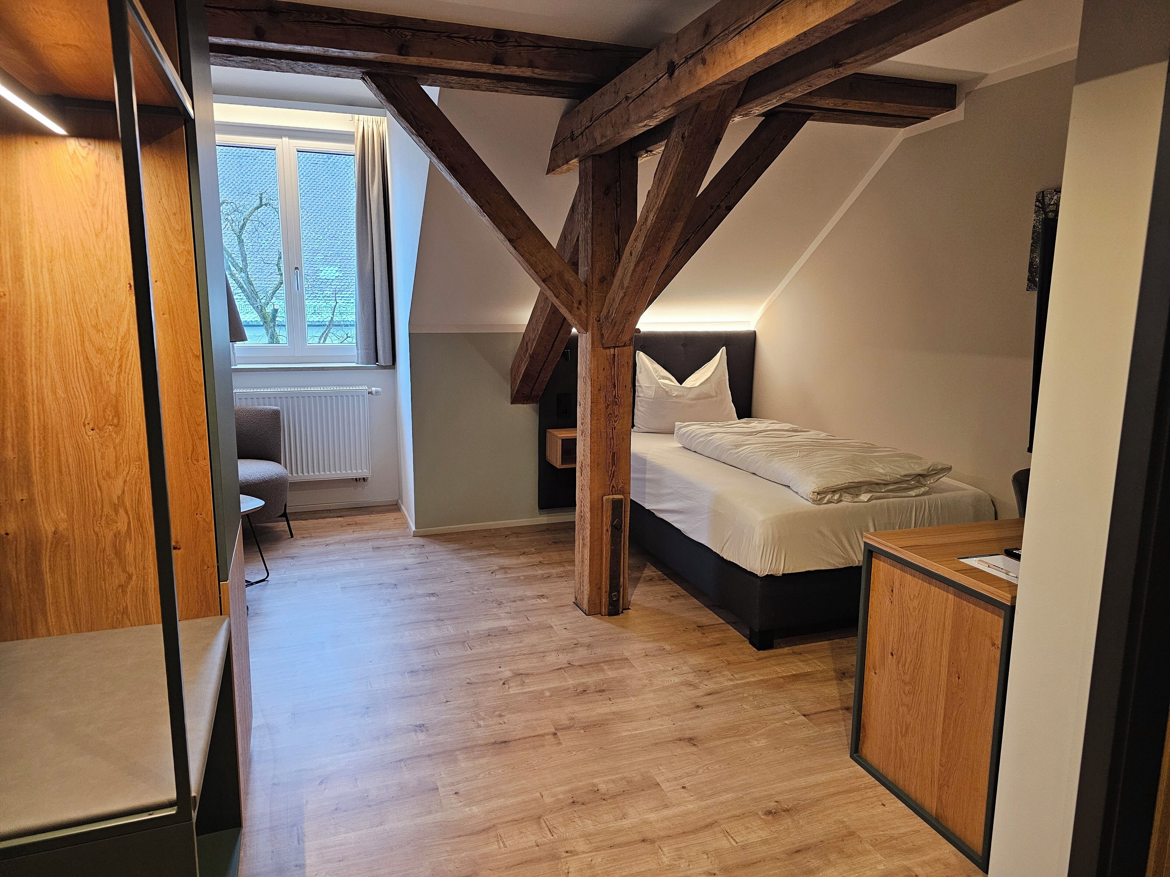 A bedroom with a sloped ceiling, a bed, a desk, and a radiator.