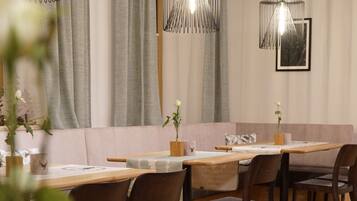 A restaurant with wooden tables and chairs, grey curtains, and hanging pendant lights.