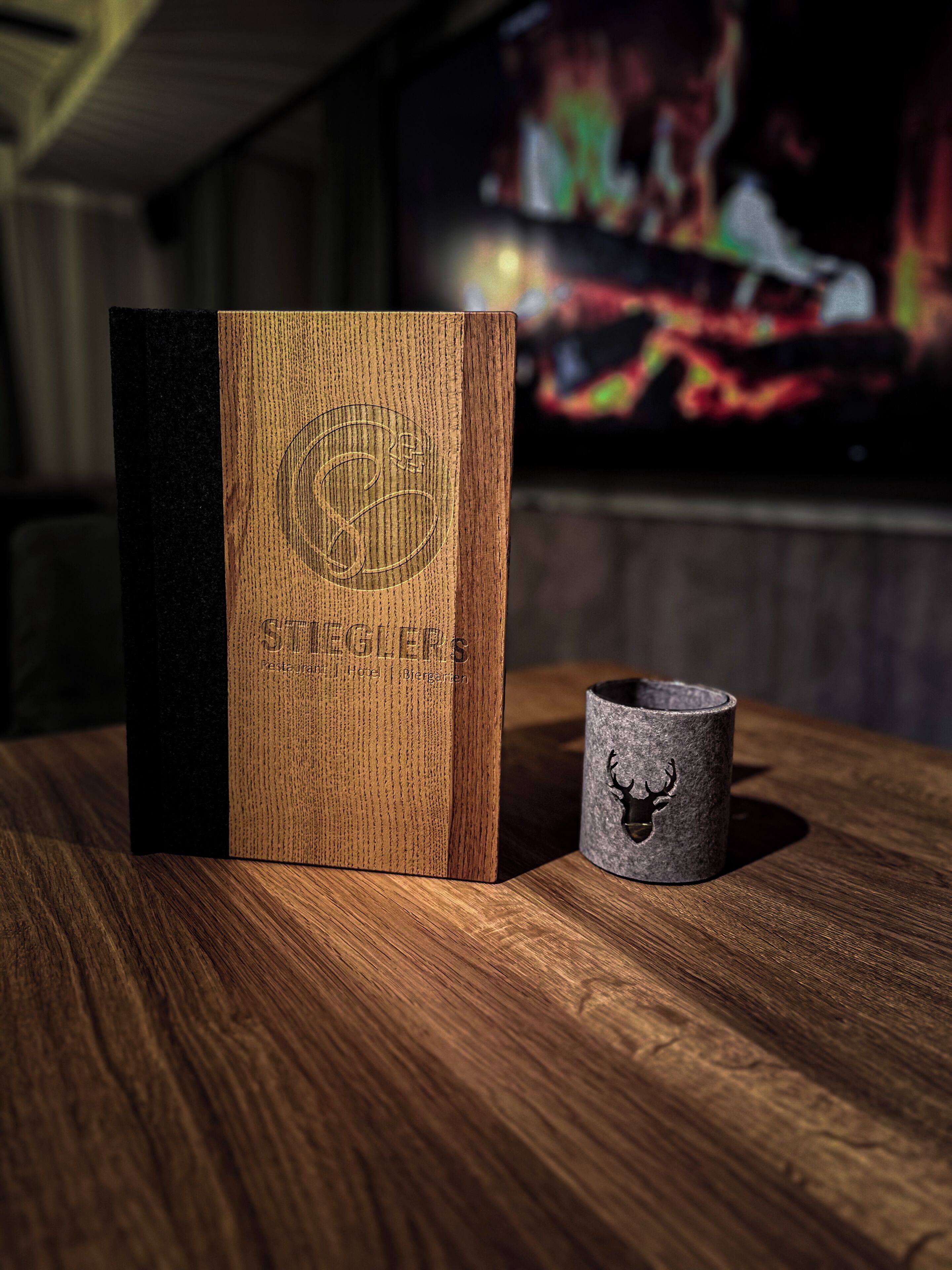 Una caja de madera con texto en relieve y una taza gris con un diseño de ciervo sobre una superficie de madera.
