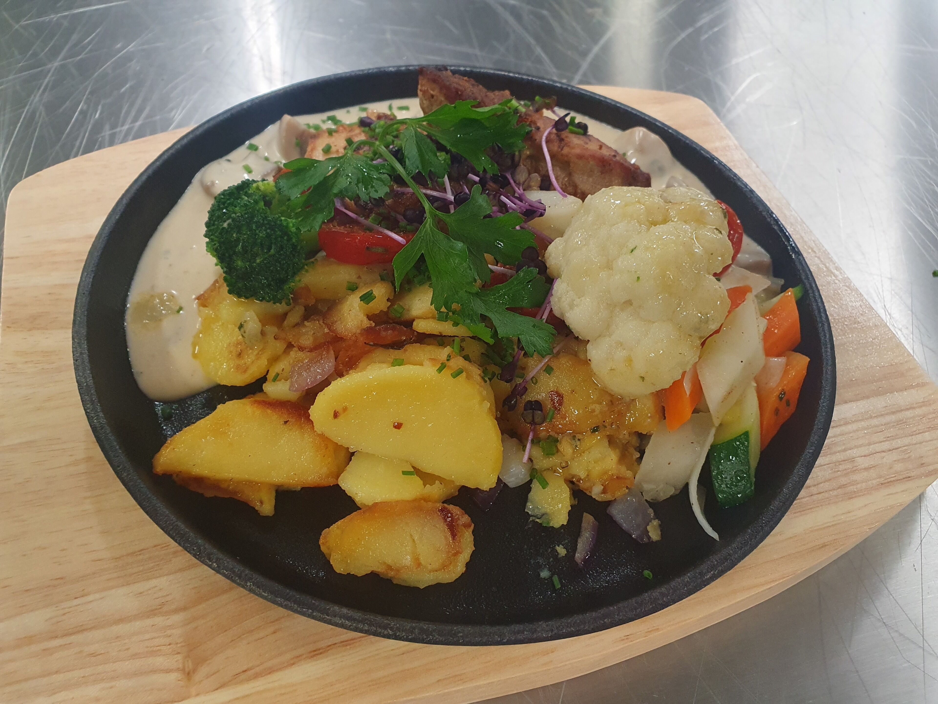 A meal with various vegetables and a piece of meat on a black plate.