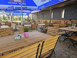 An outdoor seating area with wooden tables and chairs, blue umbrellas, and potted plants. - Stieglers - Restaurant Hotel Biergarten (Ergoldsbach)