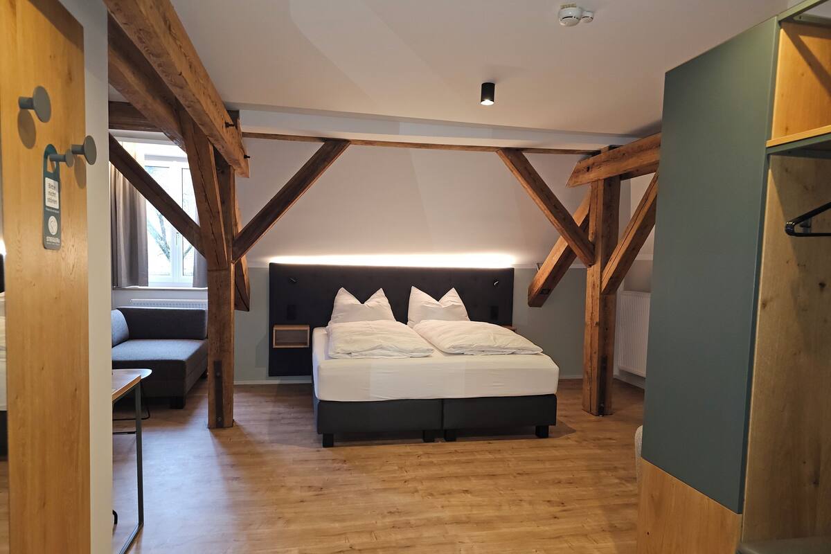 Une chambre avec un plafond en bois, un lit avec une literie blanche et une table de chevet.