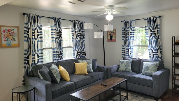 Una sala de estar con dos sofás grises, una mesa de centro de madera y cortinas estampadas.