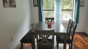 Un comedor con una mesa y sillas, un florero sobre la mesa y una ventana con cortinas.