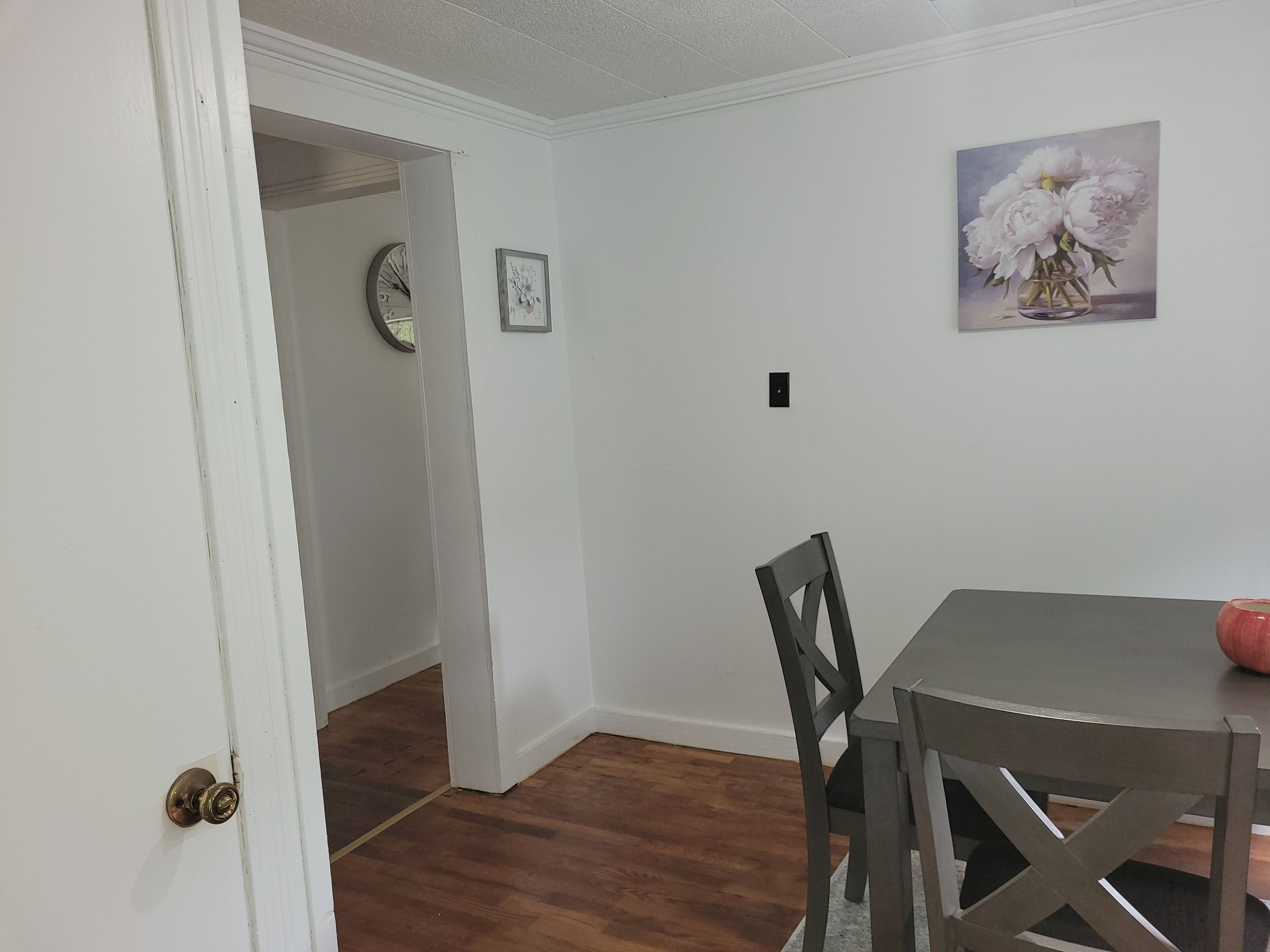 A dining area with a table and chairs, a door leading to another room, and a wall-mounted picture.