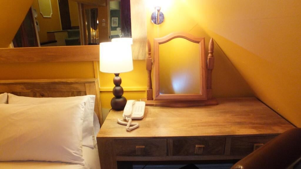 A hotel room with a wooden headboard, a bedside lamp, a telephone, and a mirror on a wooden nightstand.