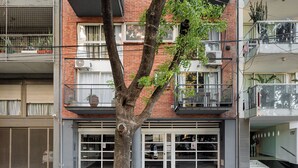 Un immeuble à plusieurs étages doté de balcons, avec un arbre au premier plan et une entrée de garage.