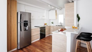 Une cuisine moderne dotée d’un réfrigérateur en acier inoxydable, de meubles en bois, d’un four encastré et d’un plan de travail blanc agrémenté de tabourets de bar.