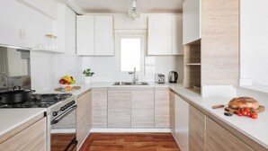 Une cuisine moderne avec des meubles blancs, un plancher en bois, une cuisinière à gaz et un évier.