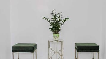 Two green cushioned stools with metal legs and a small table with a plant in a green pot.