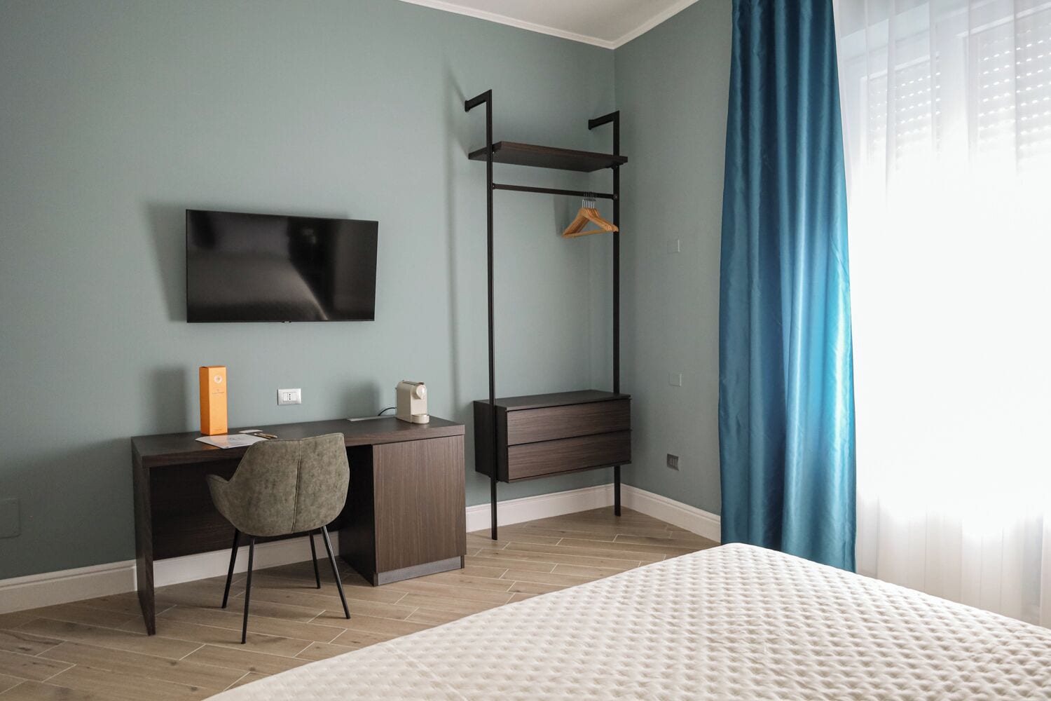 Ein modernes Schlafzimmer mit einem Bett, einem Schreibtisch mit Stuhl, einem Fernseher und einem Kleiderschrank.