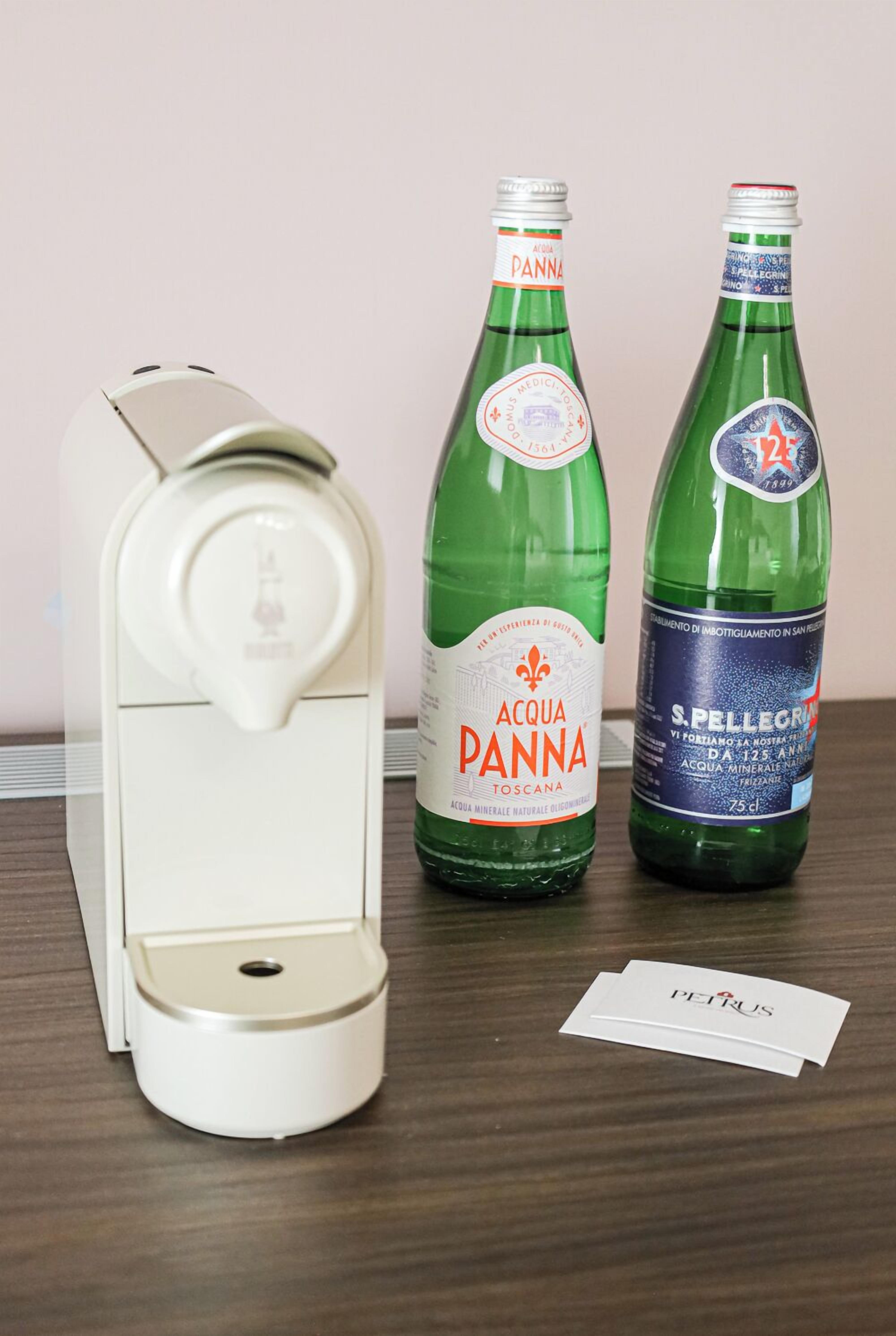 Two bottles of Acqua Panna water and a white coffee machine on a wooden table.