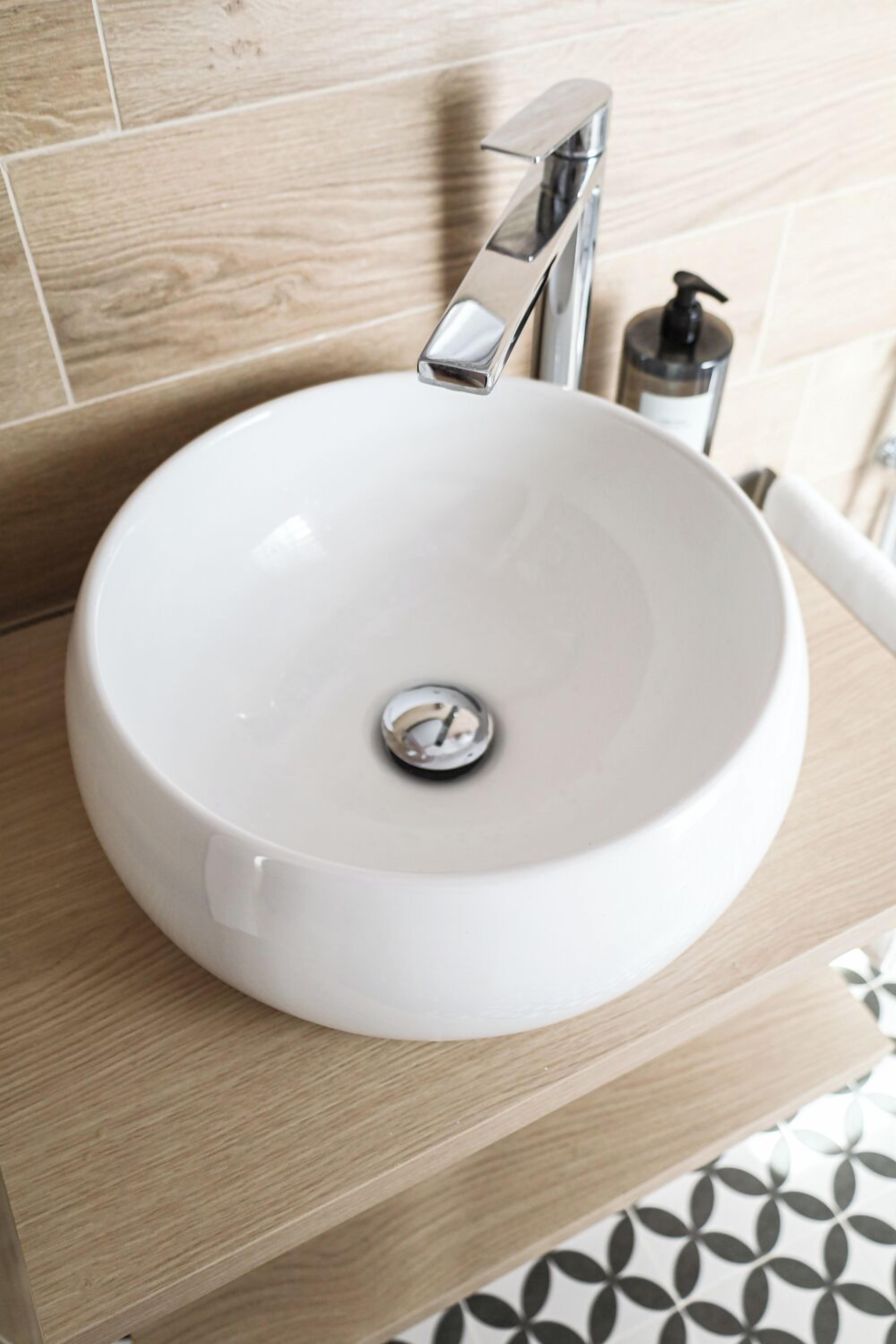 A white bathroom sink with a chrome faucet, a soap dispenser, and a drain cover.