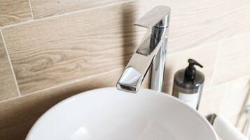 A white bathroom sink with a chrome faucet, a soap dispenser, and a drain cover.