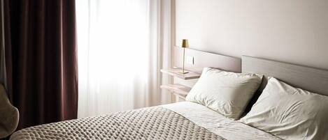 Un dormitorio con una cama grande, una mesita de noche, una lámpara y un ventanal con cortinas.