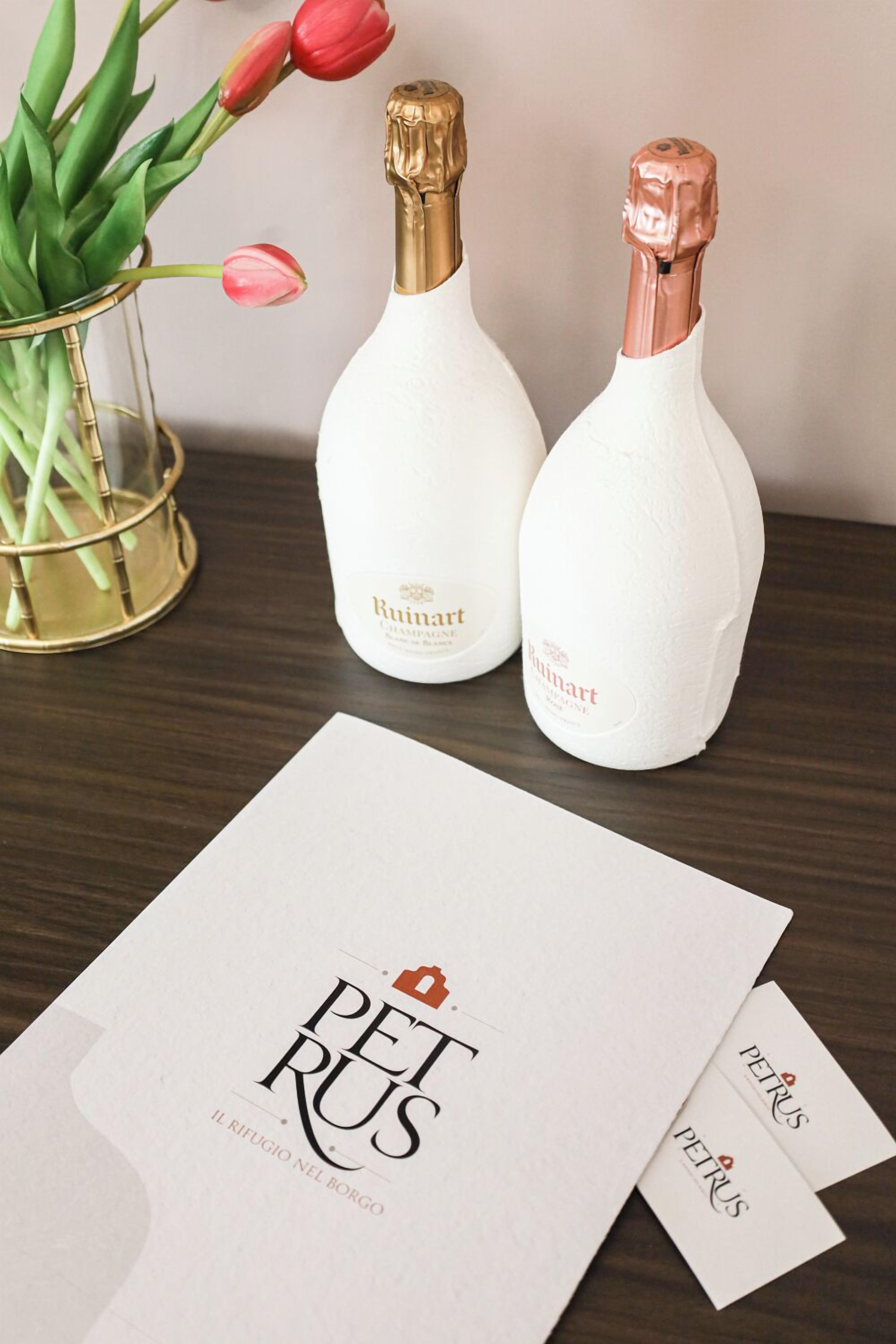 Dos botellas de champán Ruinart y una tarjeta con el texto 'PETRUS IL RIFUGIO NEL BORGO'.
