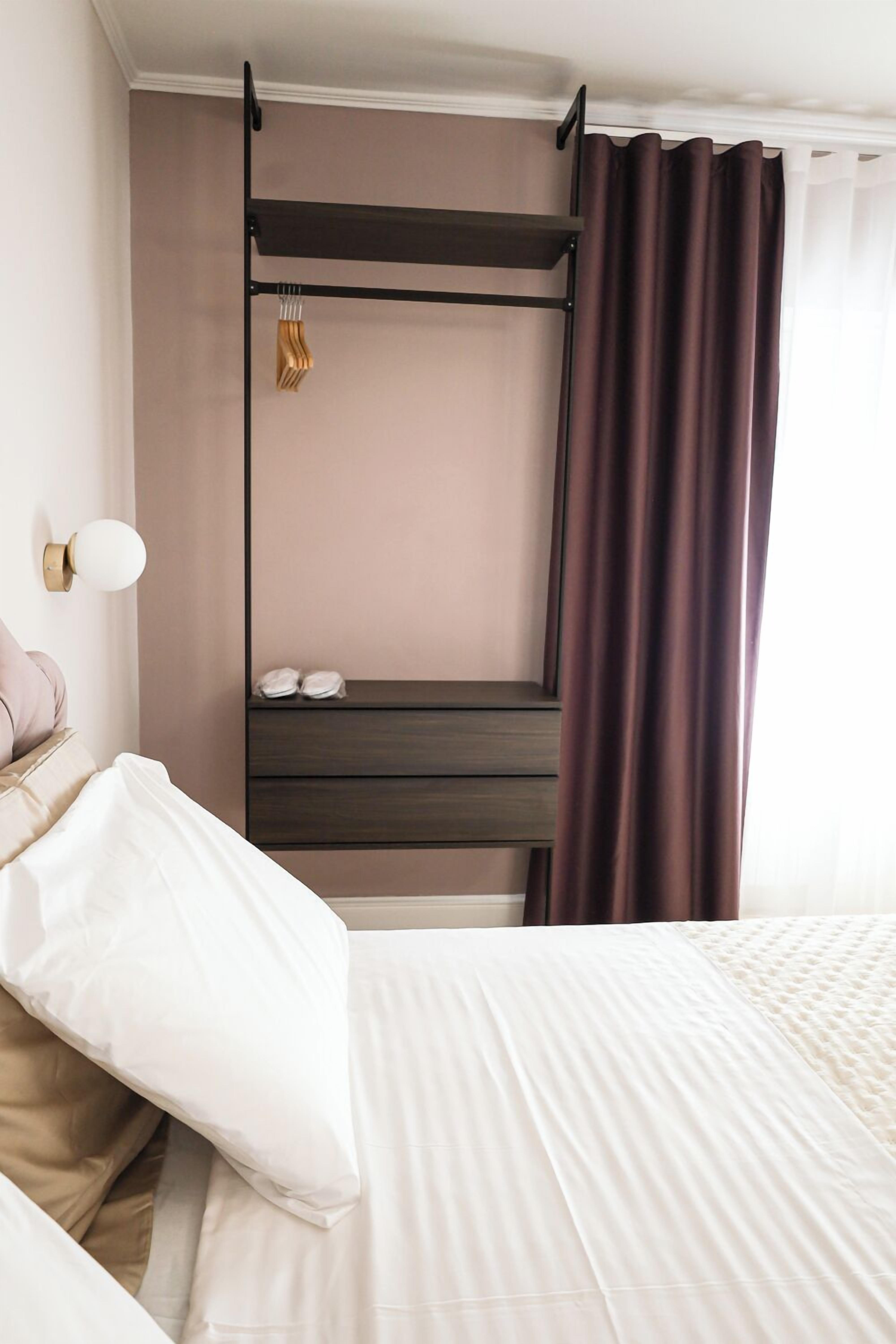Une chambre d’hôtel avec un lit, une table de chevet avec une lampe, une armoire et une fenêtre avec des rideaux.