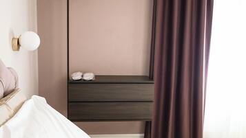Une chambre d’hôtel avec un lit, une table de chevet avec une lampe, une armoire et une fenêtre avec des rideaux.
