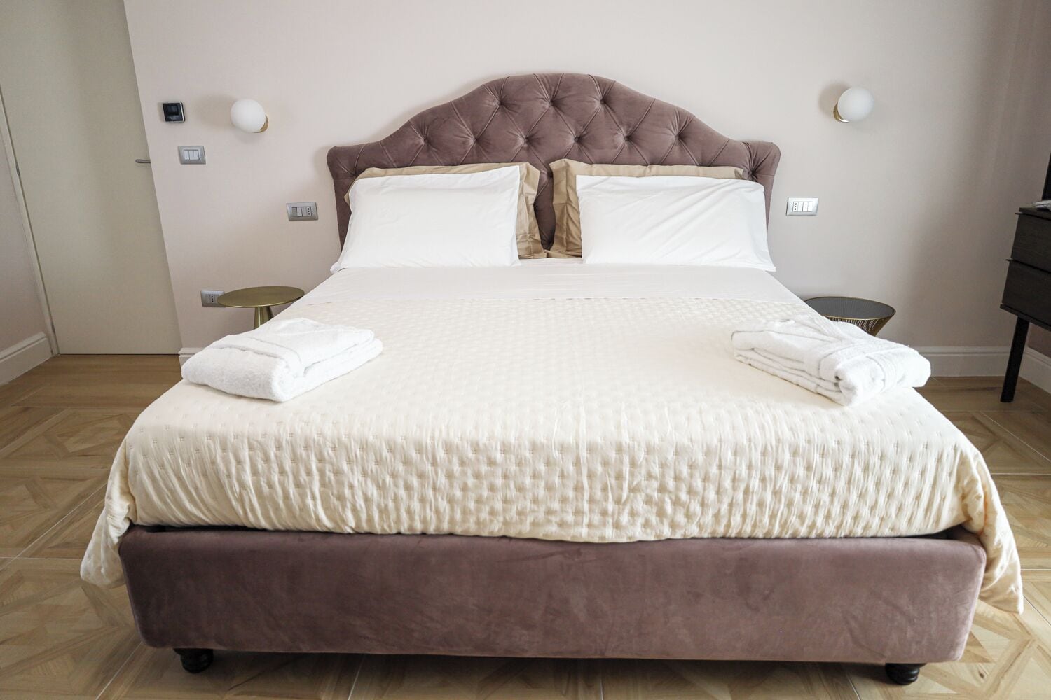 A large bed with a tufted headboard, white linens, and two folded towels on the side.