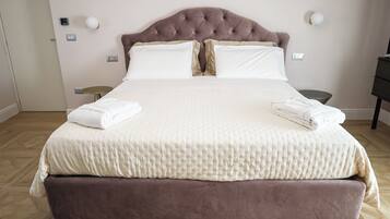 A large bed with a tufted headboard, white linens, and two folded towels on the side.