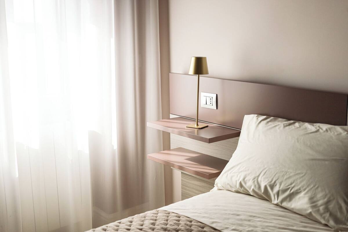 A neatly made bed with a headboard, a bedside table with a lamp, and a power outlet.