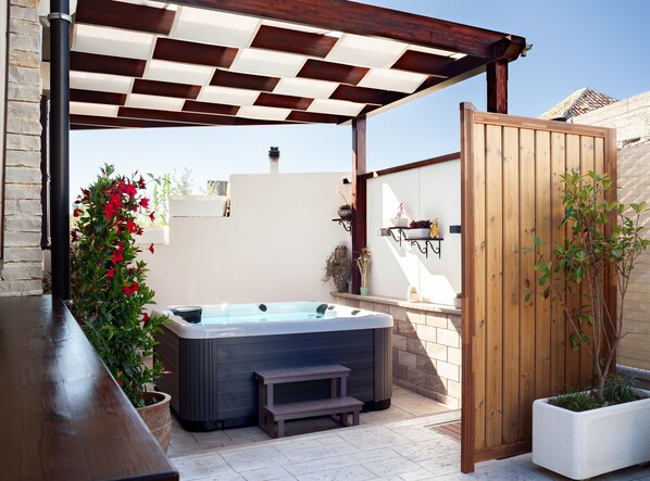 A hot tub under a wooden pergola, surrounded by potted plants and a wooden fence.
