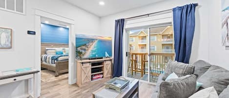 A modern living room with a sofa, a coffee table, and a TV stand. There is a painting of a coastal scene on the wall.