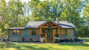 A single-story house with a stone foundation, a front porch with wooden railings, and a chimney.
