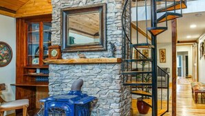 A cozy room with a stone fireplace, a blue wood stove, and a spiral staircase.