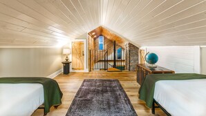 A cozy attic bedroom with two beds, a wooden ceiling, a stone wall, and a spiral staircase.