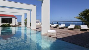 A rooftop pool area with lounge chairs labeled "Eclipse" and "St. Barth," a white building with a red roof, and a clear view of the ocean. - Villa Eclipse (Vitet)