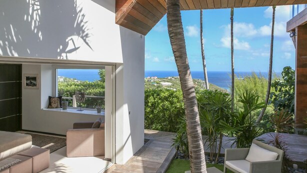 A modern living room with a large window overlooking a coastal view, furnished with a sofa and a coffee table. - Villa Eclipse (Vitet)