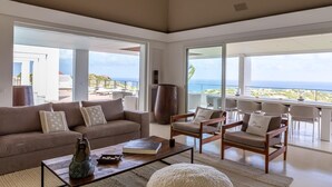 A spacious living room with a large sofa, armchairs, and a coffee table. There is a view of the ocean through large windows. - Villa Eclipse (Vitet)