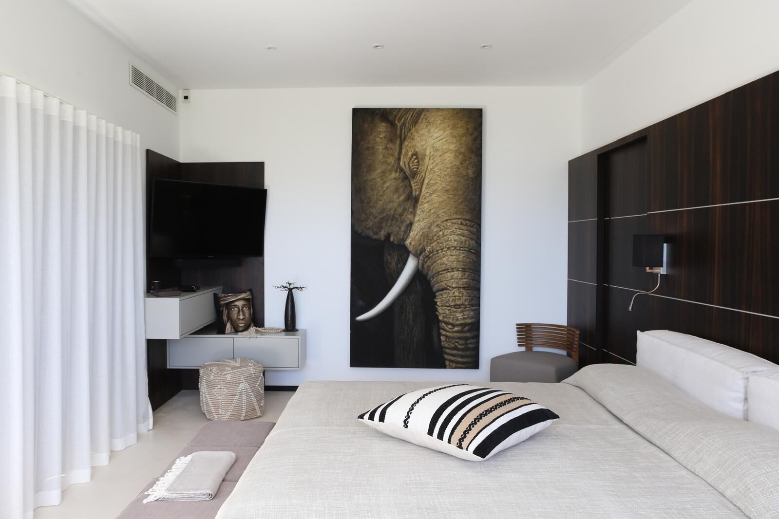 Een moderne slaapkamer met een groot kunstwerk van een olifant, een televisie, een nachtkastje en een bank.