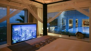 A bedroom with a cityscape view on the TV, a bed, a window with sheer curtains, and a view of a modern building outside. - Villa Eclipse (Vitet)