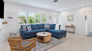A living room with a blue sectional sofa, a round wooden coffee table, and wicker chairs.