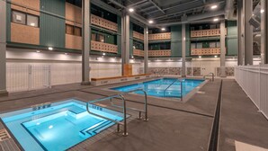 An indoor swimming pool with two lanes, surrounded by a high ceiling with visible ductwork and a balcony with a railing. - Winter Escape On Perfection, Ski In/Out, Pool and Hot Tub (Big White)