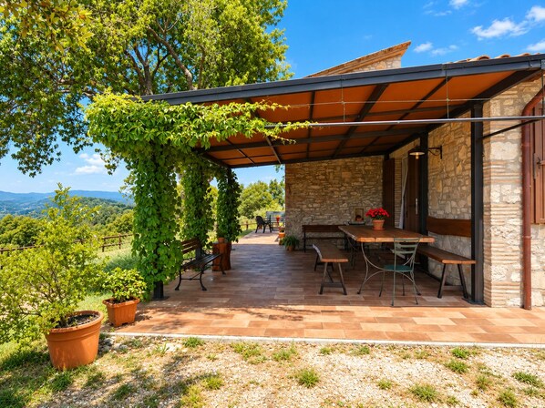 A covered outdoor patio with stone walls, a wooden table, benches, and potted plants.