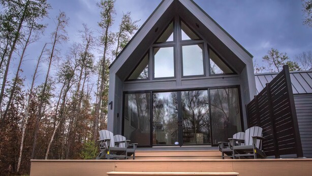 A modern house with a large glass front, two chairs on the porch, and a number '1' on the wall. - Modern Forest Chalet • Sleeps 6 • Starlink • Rivers & Caberfae • Pet-Friendly (Wellston)