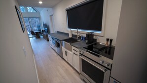 A modern kitchen with a large window, built-in appliances, and a dining area visible in the background. - Modern Forest Chalet • Sleeps 6 • Starlink • Rivers & Caberfae • Pet-Friendly (Wellston)