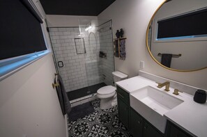 Een kleine badkamer met een wit toilet, een douchecabine, een wastafel met gouden kraan en een grote spiegel met gouden lijst.