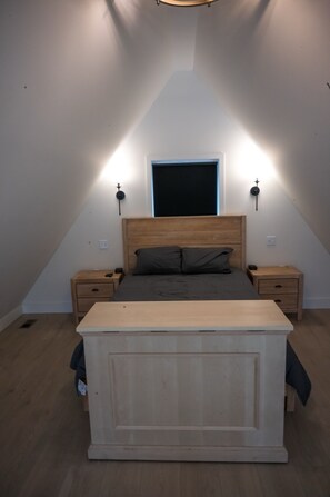 Een slaapkamer met een schuine plafond, een bed met houten hoofdbord, twee nachtkastjes en wandlampen.