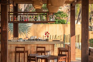 A wooden bar area with a variety of liquor bottles, a bar counter, and seating. - Casa Yati (Santa María Tonameca)