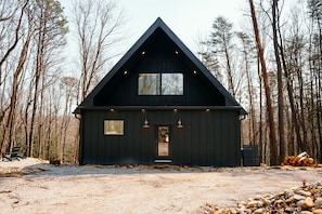 A cabin with a triangular roof, a front door with a wreath, and a gravel driveway.