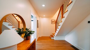 A modern interior with a wooden staircase, a white wall, and a wooden bench with a potted plant.
