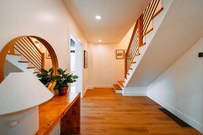 A modern interior with a wooden staircase, a white wall, and a wooden bench with a potted plant.